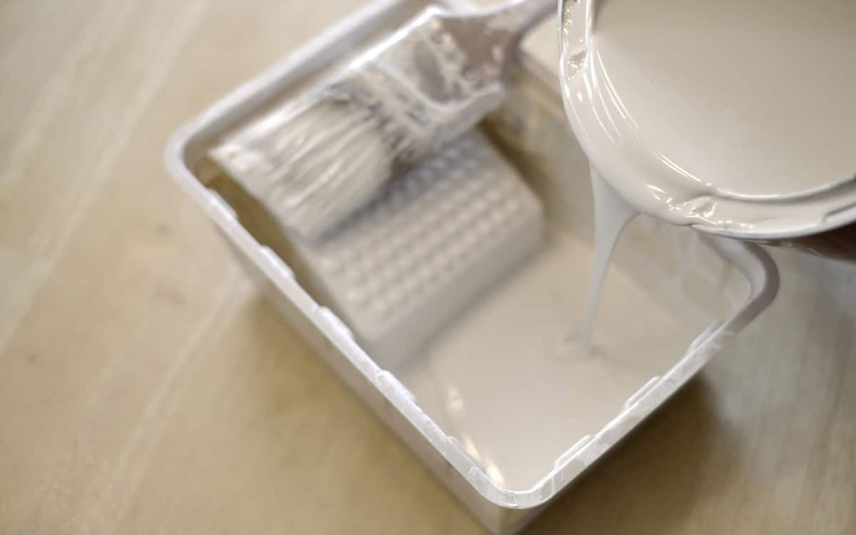 Pouring white paint into plastic paint bin with paintbrush for painting home