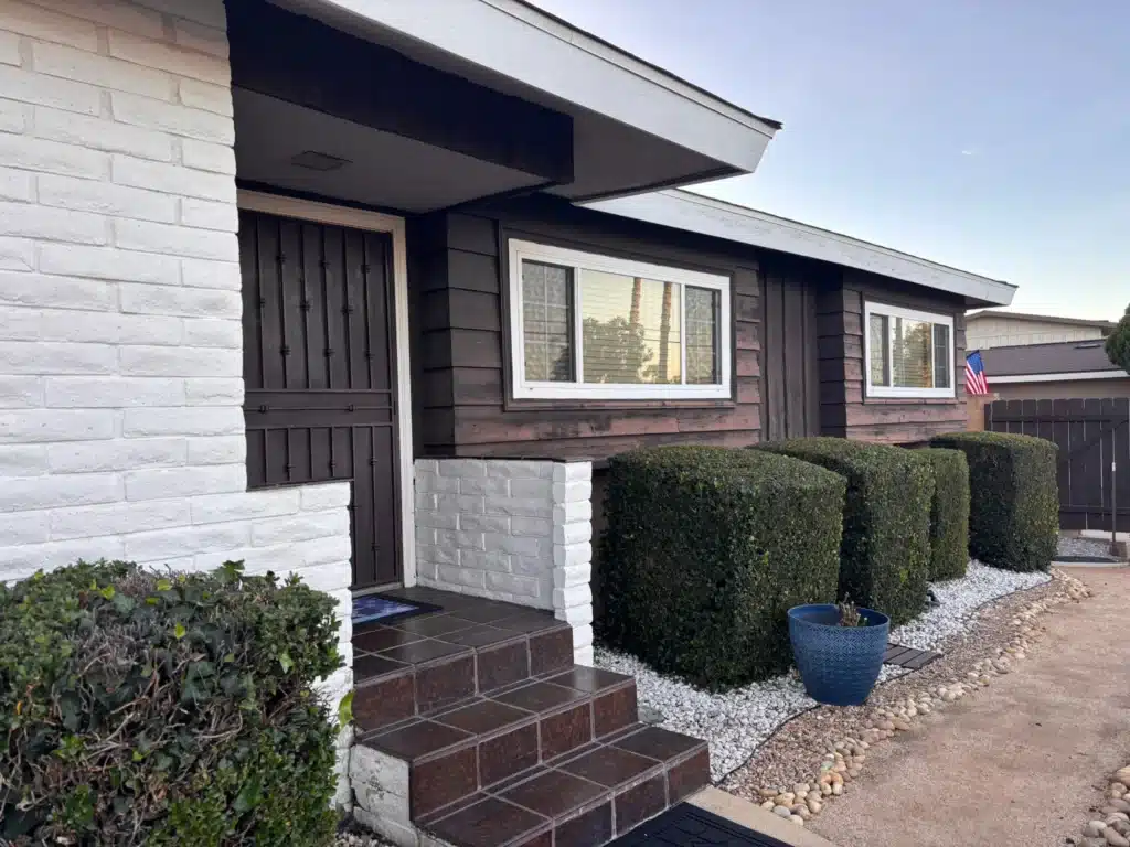 Exterior Home Painting with Dark Siding and White Brick Accents The front entrance of a house featuring dark brown siding, white painted brick, and a dark brown door.