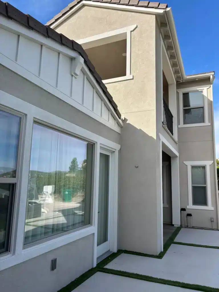 Modern Home Exterior Painting with Stucco and White Trim The side of a modern two story house with light beige stucco and crisp white trim.