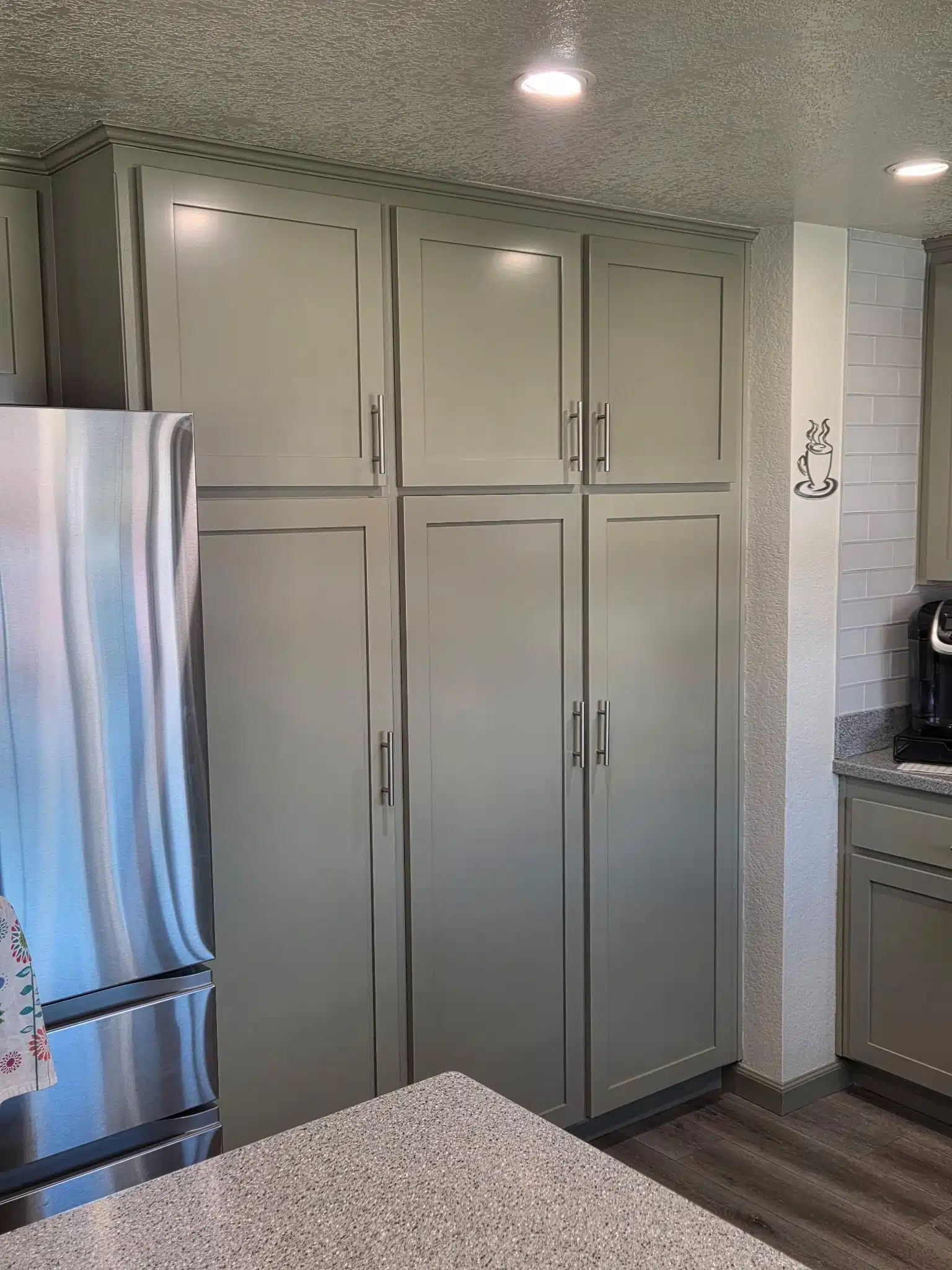 Tall Kitchen Cabinets Painted Sage Green for Modern Kitchen Tall kitchen cabinets freshly painted in a modern sage green color next to a stainless steel refrigerator.