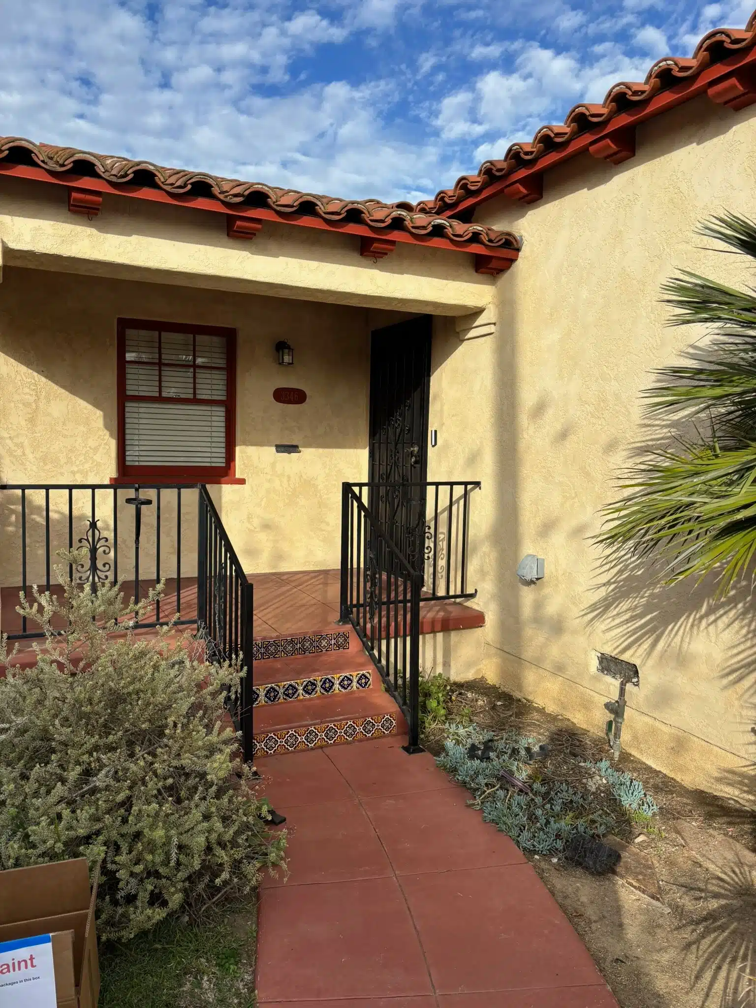 Spanish Style Home Exterior Painting with Red Tile Roof Spanish style home entrance with light yellow stucco, red tile roof, and black wrought iron gate.