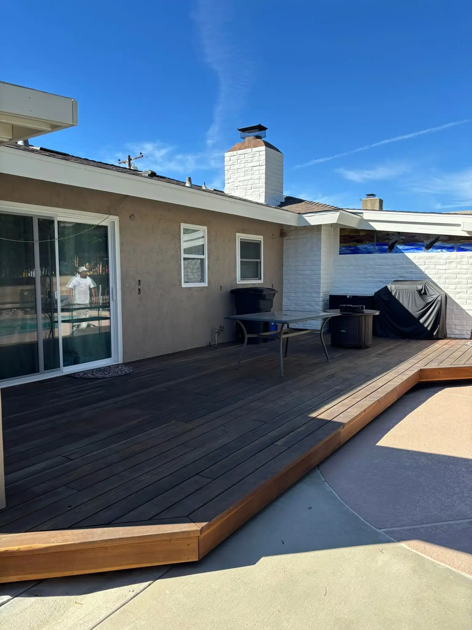 Backyard Patio with Wooden Deck and Painted Stucco Exterior Spacious backyard patio featuring a large wooden deck, sliding glass door, and a house with light brown stucco exterior.