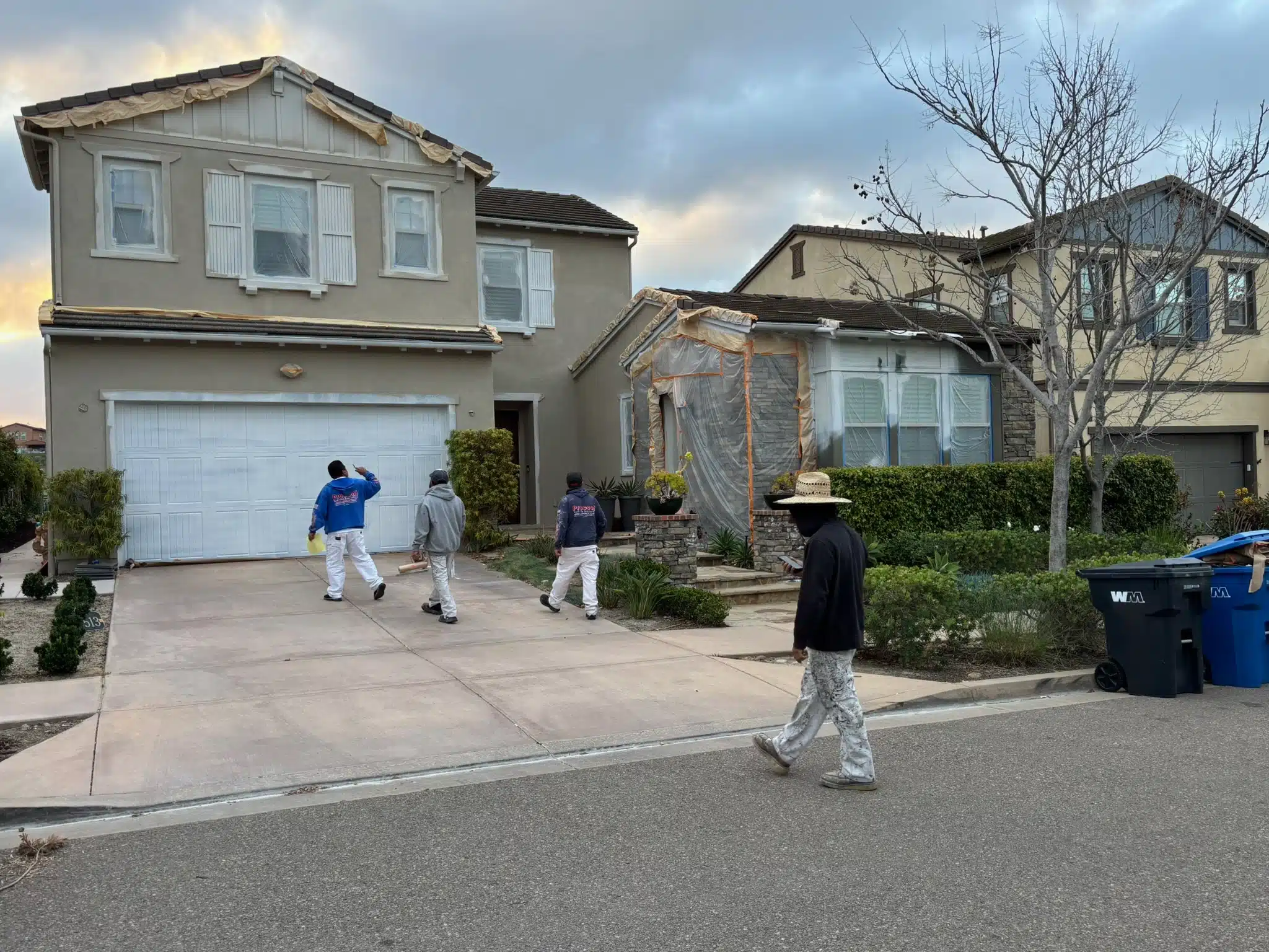 Professional Painting Crew Prepping House for Exterior Paint A professional painting crew walks on the driveway, preparing a residential house for exterior painting services.