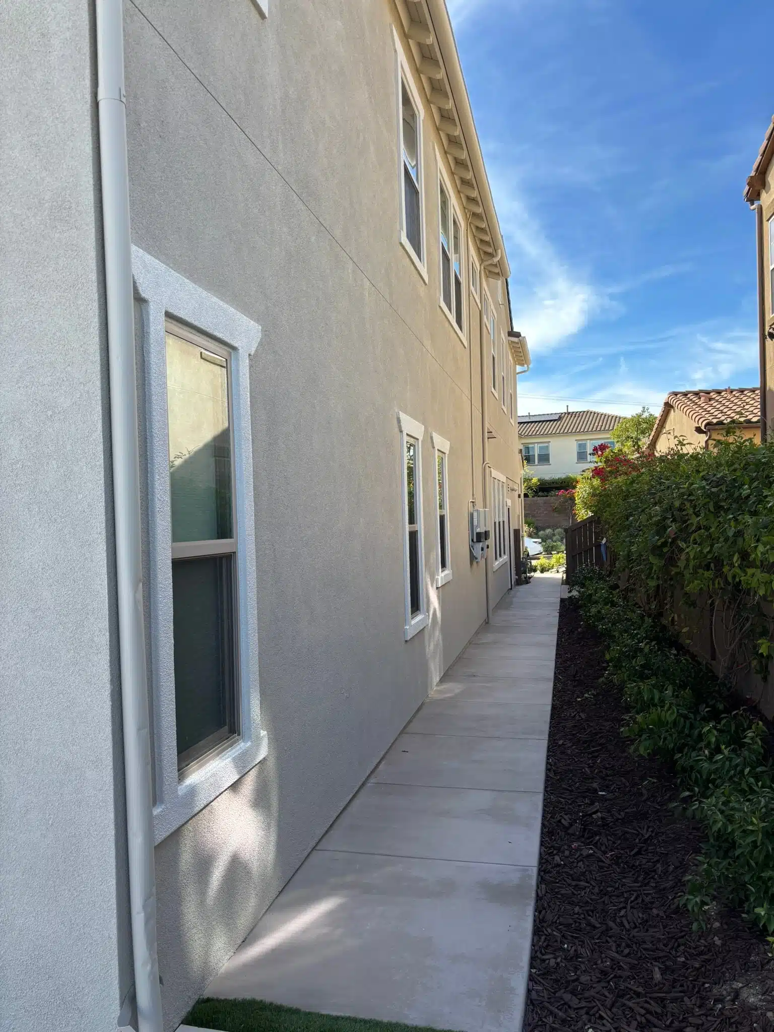 Freshly Painted Stucco Exterior with White Window Trim Side view of a residential house with newly painted light gray stucco and crisp white window trim.