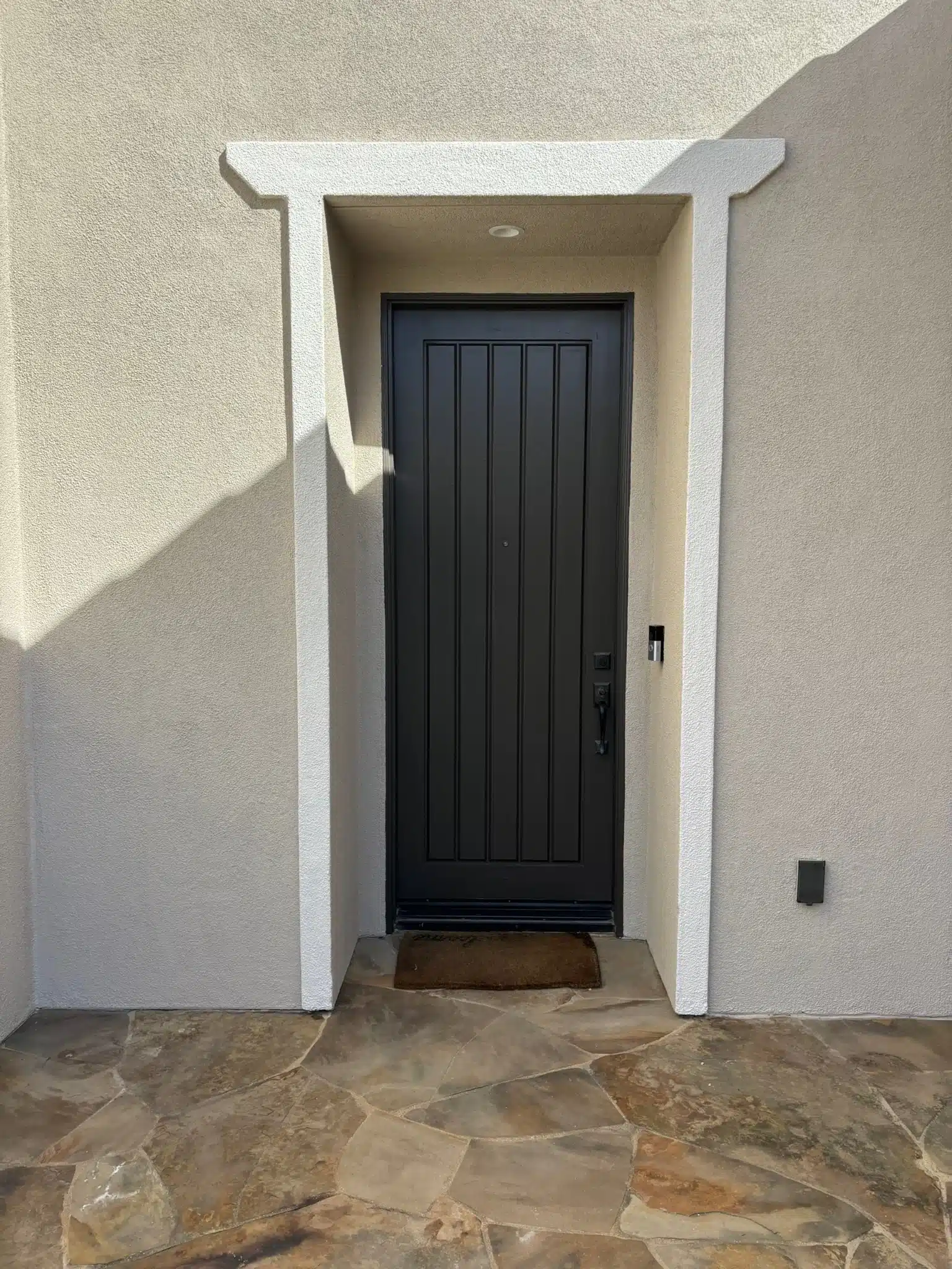 Modern Black Front Door Painting with White Trim Newly painted modern black front door with vertical panels and white trim on a stucco wall.