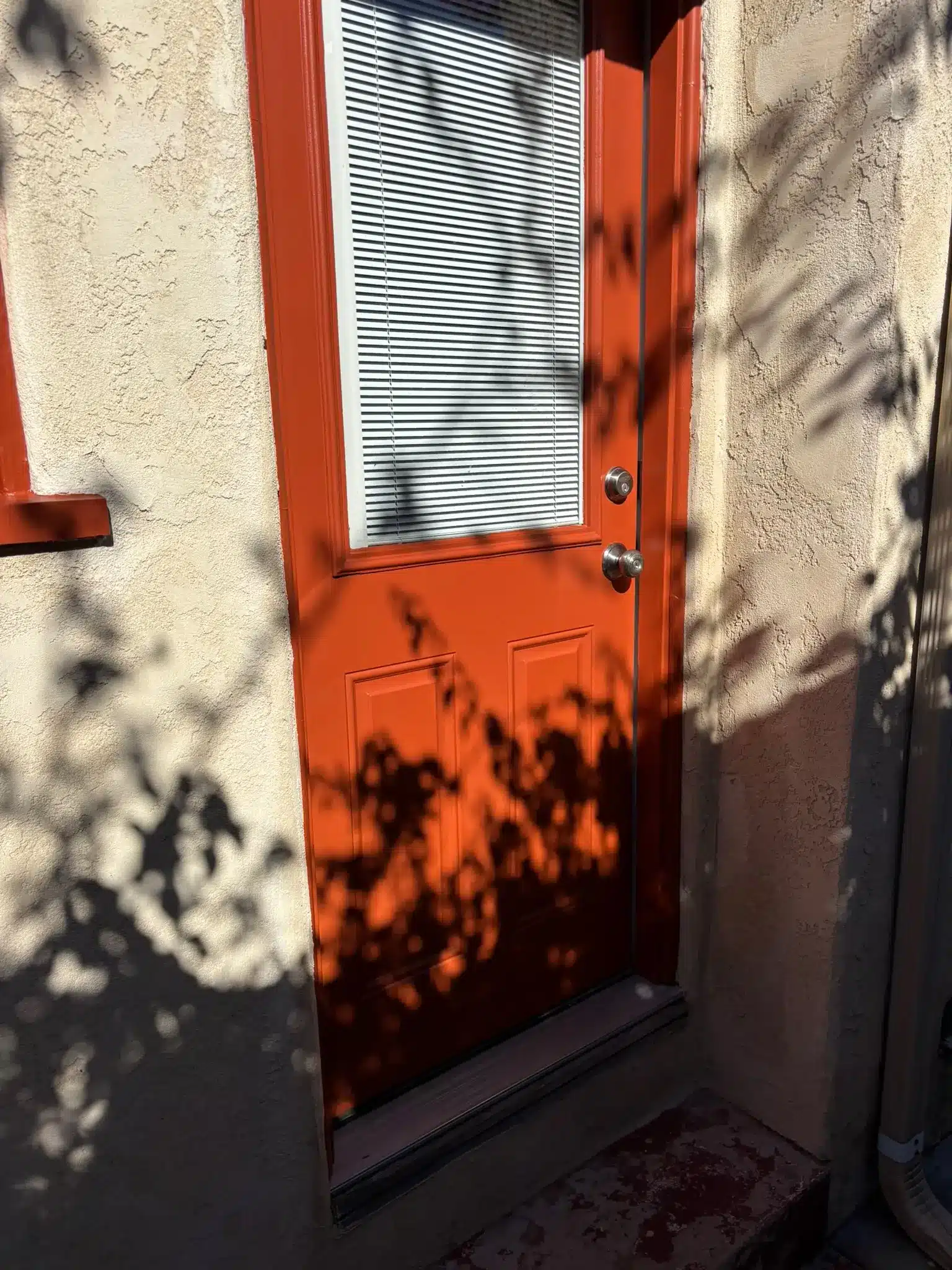 Vibrant Orange Exterior Door Painting Service A freshly painted vibrant orange exterior door with a window and blinds, enhancing home curb appeal.