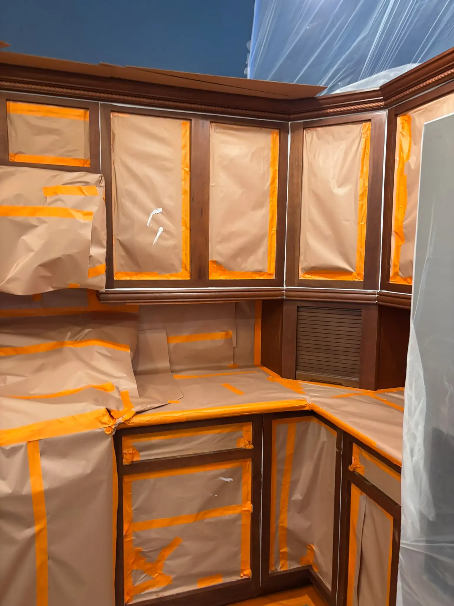 Professional Kitchen Cabinet Painting Preparation Kitchen cabinets meticulously prepped with paper and tape for a professional, clean cabinet painting project.