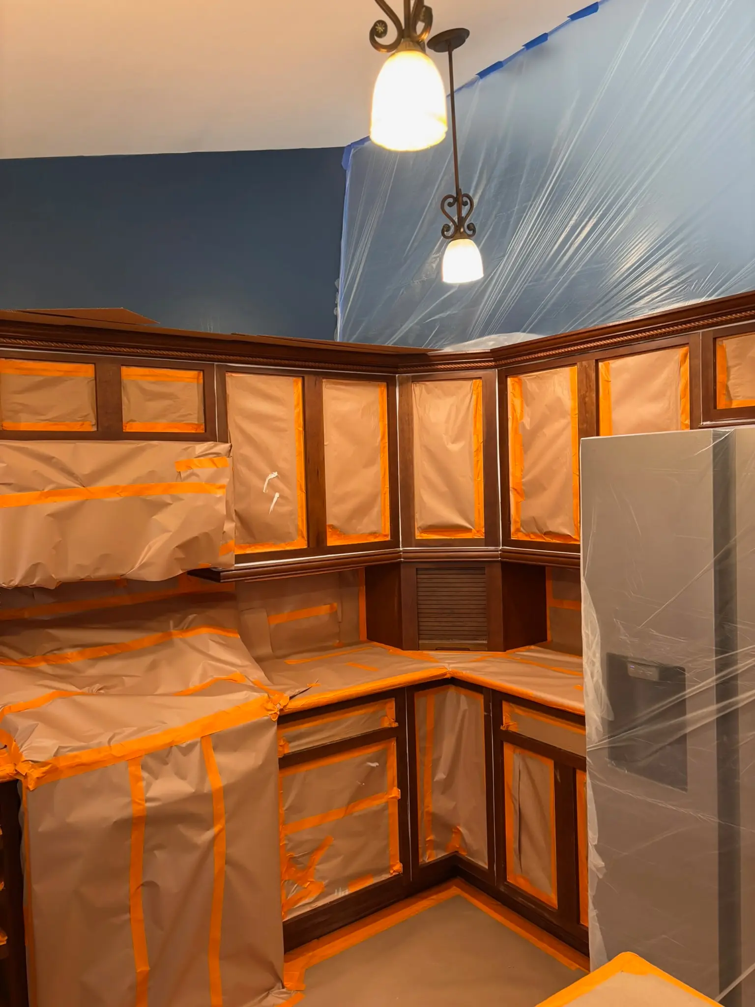 Kitchen Cabinet Painting Project Preparation Kitchen cabinets meticulously prepped with paper and tape for a professional, clean cabinet painting project.