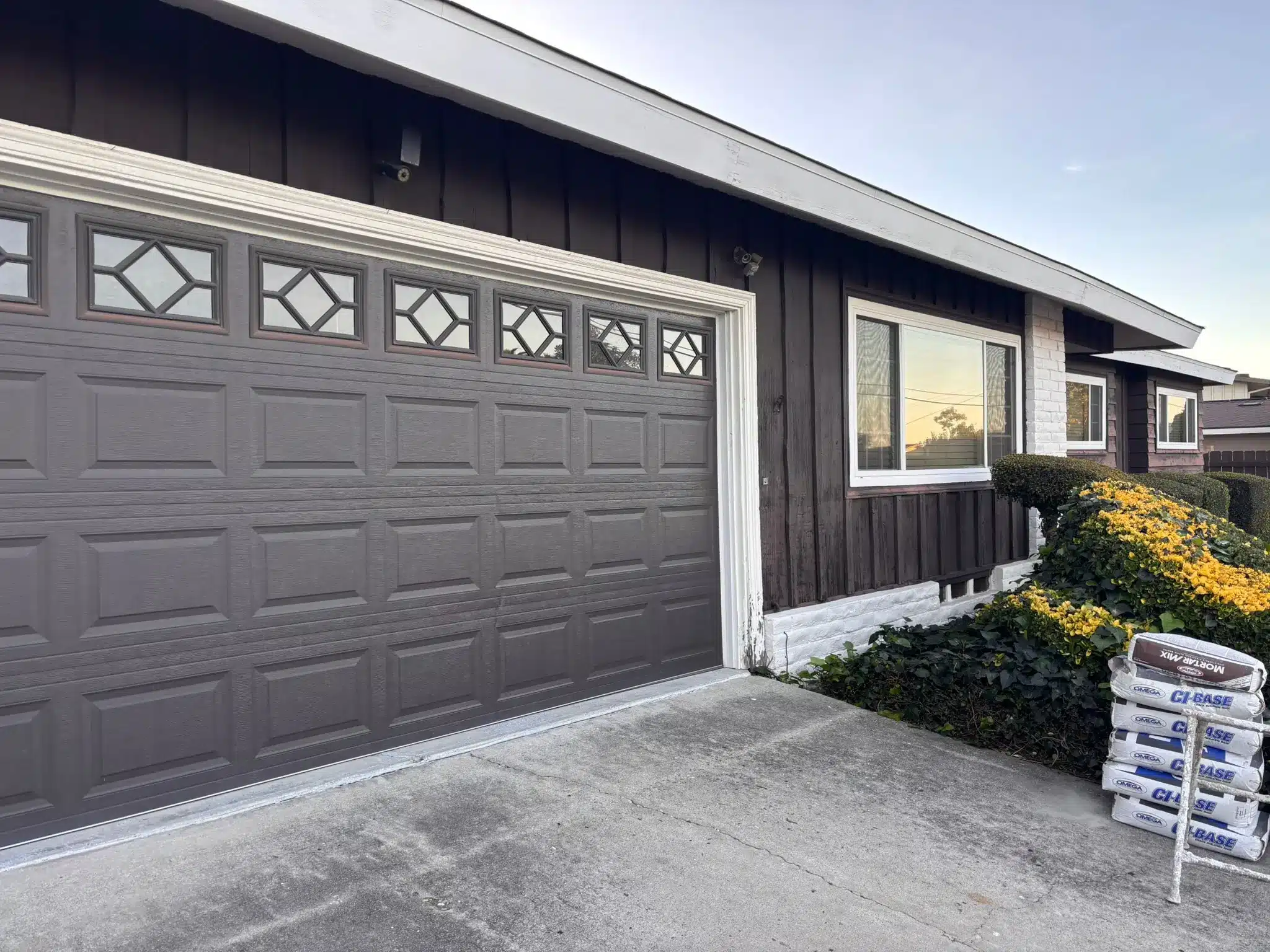 Exterior House Painting and Garage Door Refresh A residential house exterior with dark brown siding and a freshly painted gray garage door, enhancing curb appeal.