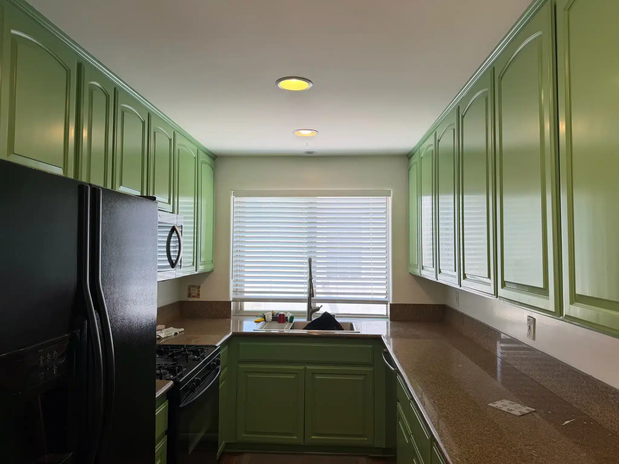 Galley Kitchen Cabinet Painting Transformation A beautifully painted galley kitchen with bright green cabinets, granite countertops, and a window above the sink.